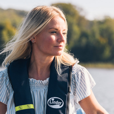 Blond vacker kvinna som bär flytväst sitter i en båt en sommardag.